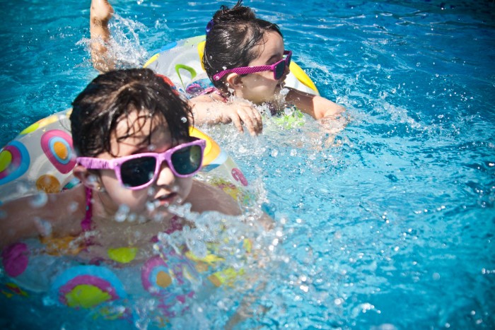 Two girls with sunglasses swimming in a pool - swimming is one way to encourage kids to spend more time outdoors
